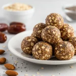 A plate of homemade energy balls made with oats, chia seeds, and dates, with almonds and ingredients scattered around.