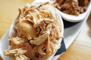 Close-up of shredded rotisserie chicken served on a white platter.