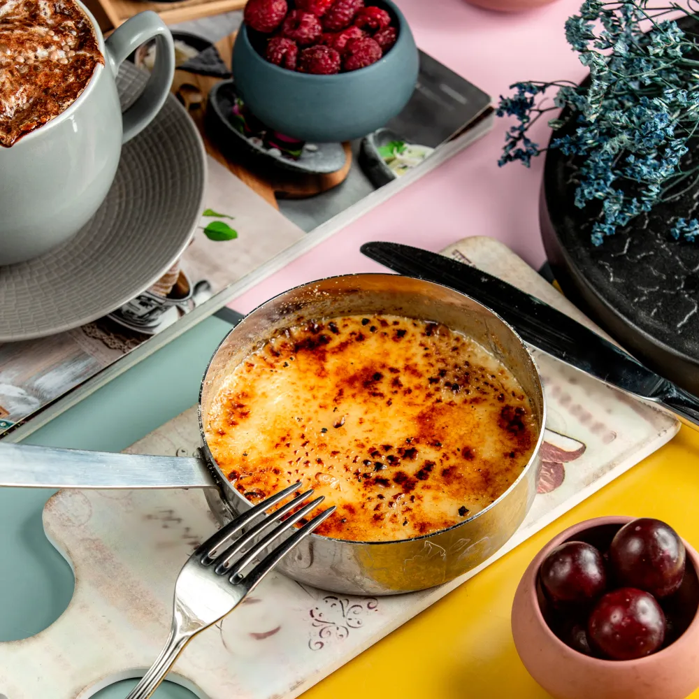 Crab Brulee served in a metal ramekin with caramelized sugar topping, surrounded by berries, coffee, and decorative plates