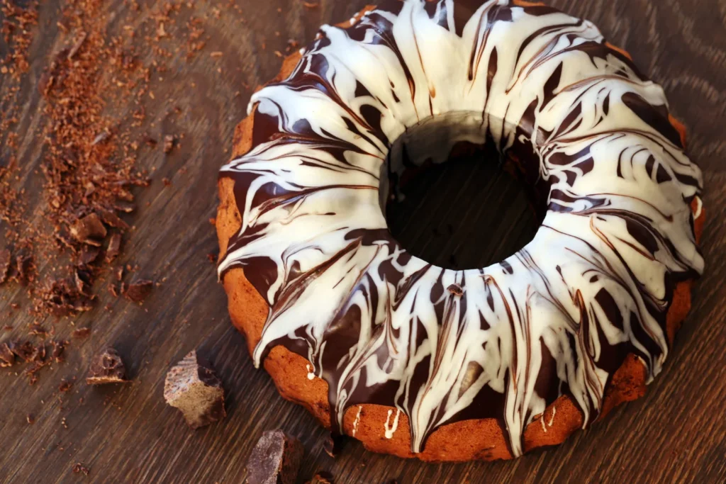 Chocolate cream cheese pound cake with a marble chocolate and vanilla glaze, served on a wooden table with chocolate shavings.