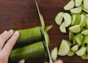 Slicing fresh cucumbers on a wooden cutting board for salad.