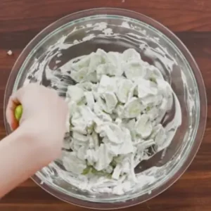 Mixing creamy cucumber salad in a glass bowl with fresh dressing