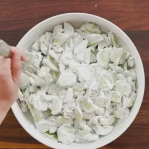 A bowl of creamy cucumber salad being stirred with a fork.