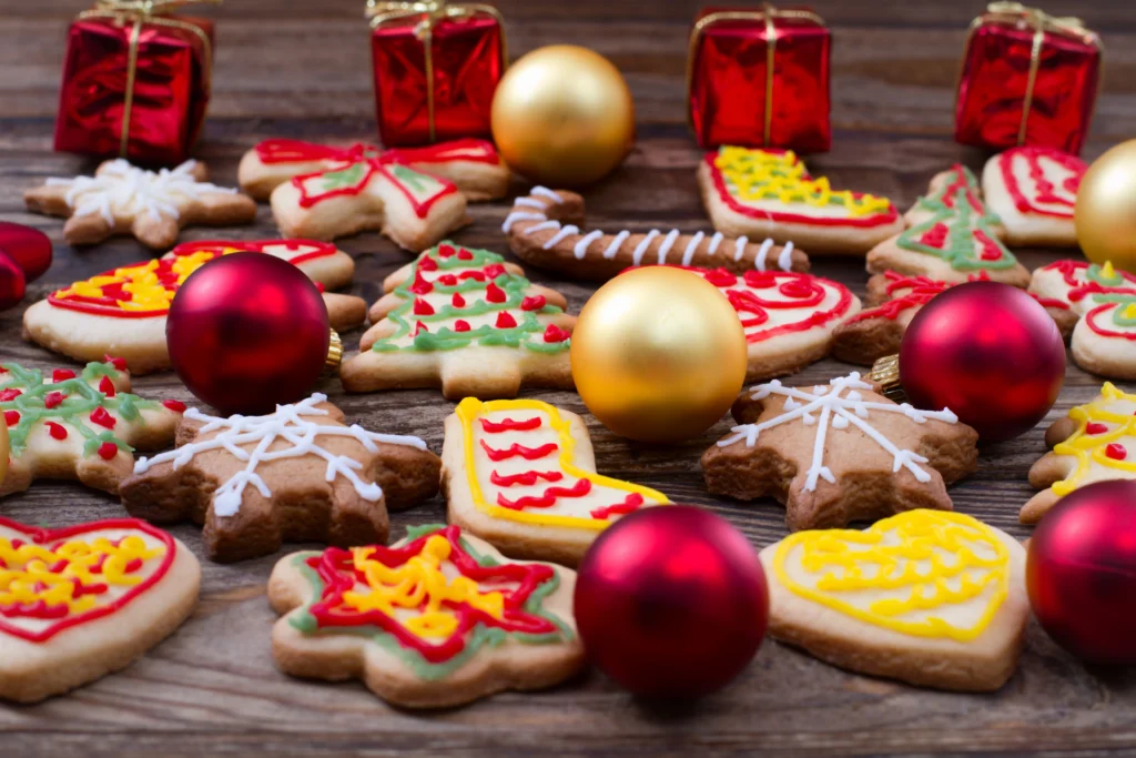 Festive Christmas cookies decorated with icing alongside red and gold ornaments on a wooden table