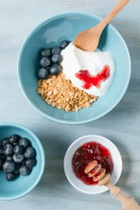 Gluten-free dairy-free breakfast with granola, blueberries, dairy-free yogurt, and strawberry jam in a blue bowl