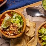 A vibrant bowl of Taco Soup Frios served with lime, lettuce, and tortilla chips, showcasing fresh ingredients and chilled taco flavors.