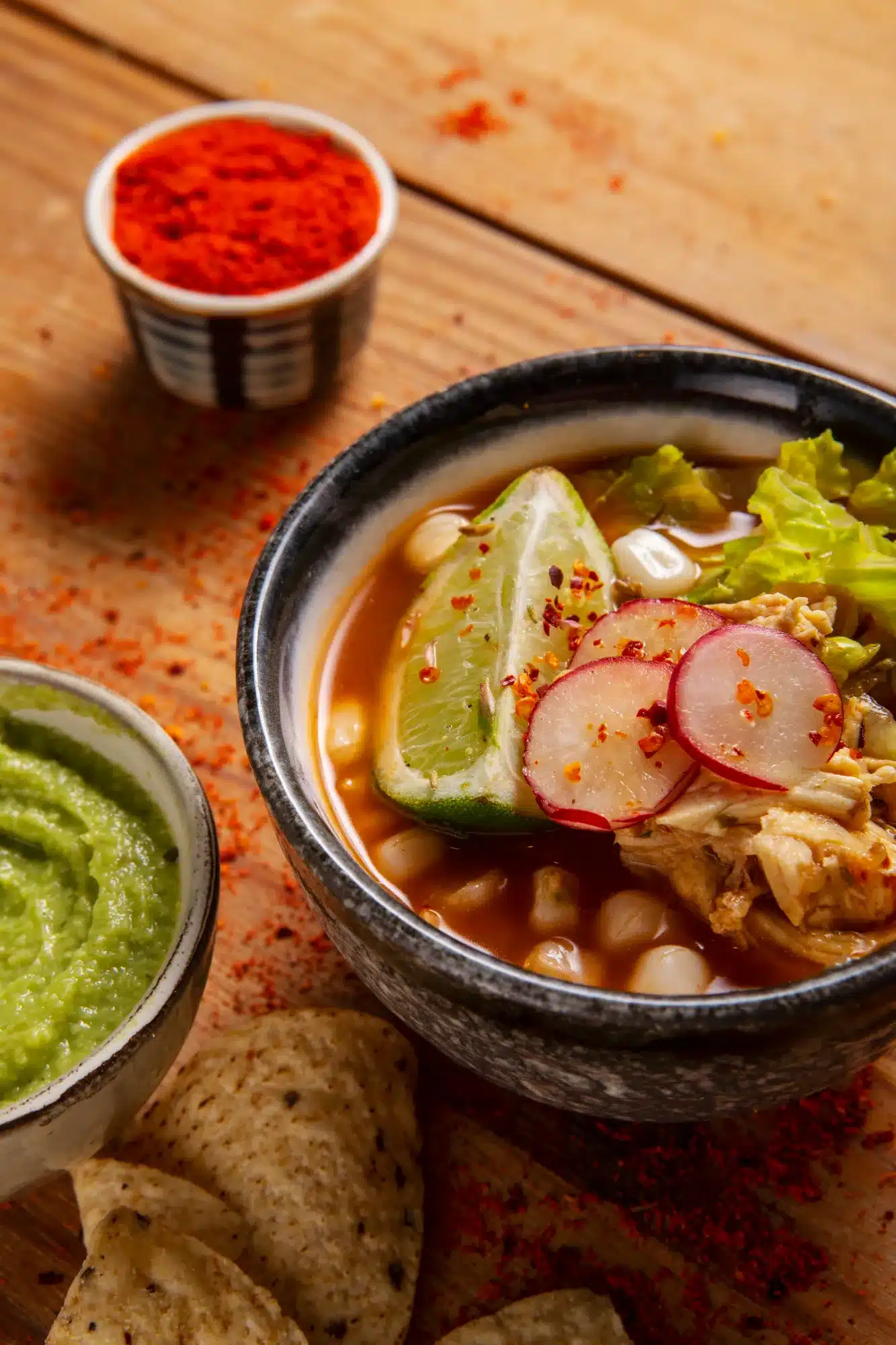A bowl of Taco Soup Frios Recipe garnished with lime, radish slices, and lettuce, served with guacamole and tortilla chips on the side.