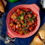 Colorful bowl of canned corned beef breakfast recipe with bell peppers, garnished with parsley, served on a rustic table with bread and a green drink.