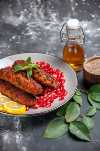 A plate of crispy, golden fish prepared with a fish fry seasoning recipe, garnished with pomegranate seeds, lemon slices, and mint, with seasoning ingredients nearby