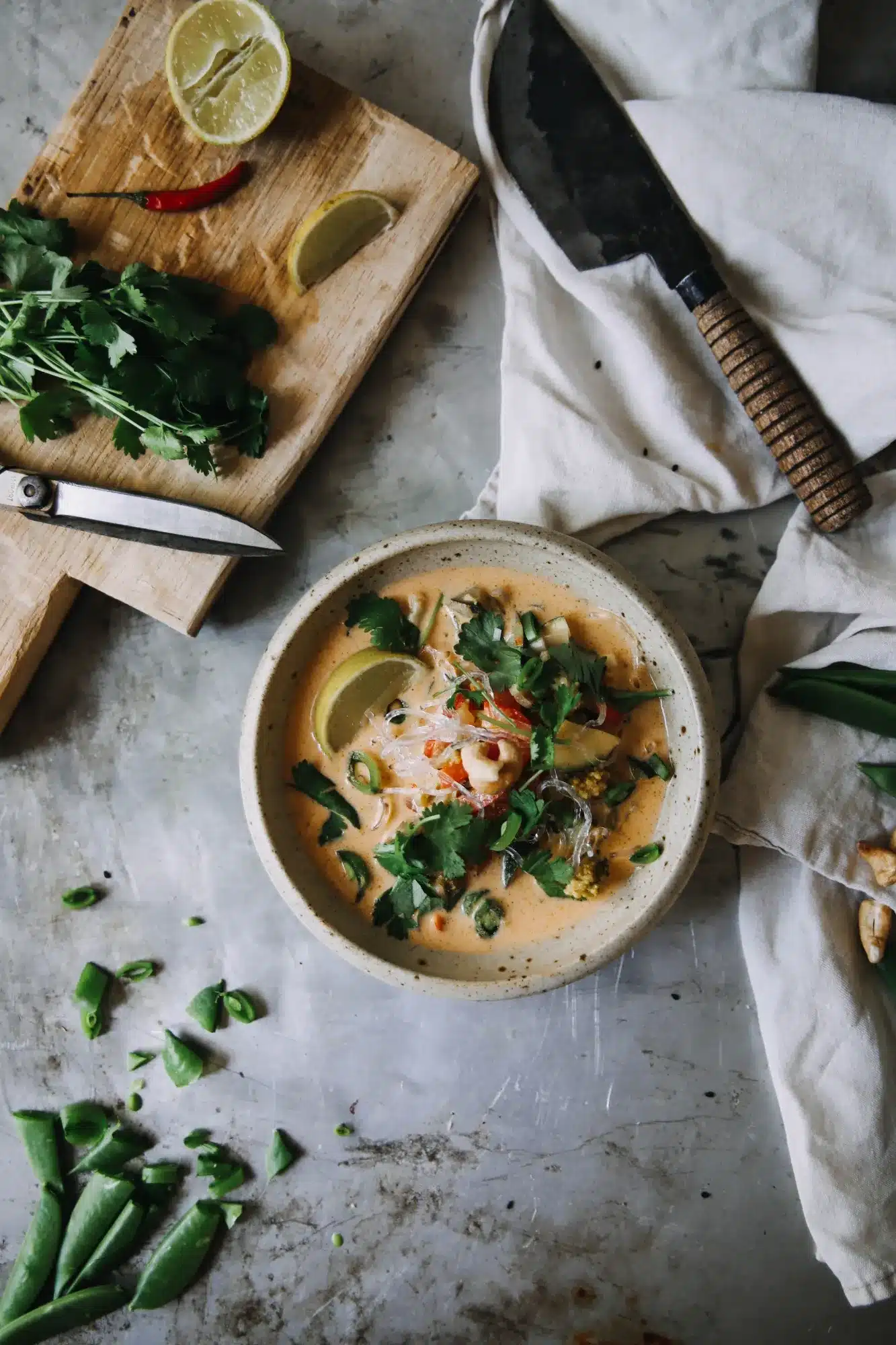 A bowl of spicy langostino sauce garnished with fresh herbs, lime, and chili, surrounded by vibrant ingredients on a rustic surface.