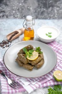 Stuffed grape leaves served with lemon and mint, accompanied by olive oil and yogurt, ideal for pairing with French rognon dishes.