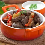 Beef kidney recipe served in a bright orange bowl with peppers and potatoes in a rustic setting.