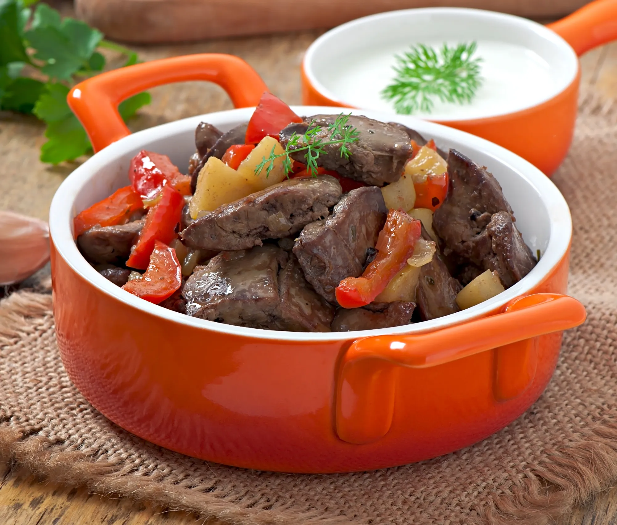 Beef kidney recipe served in a bright orange bowl with peppers and potatoes in a rustic setting.