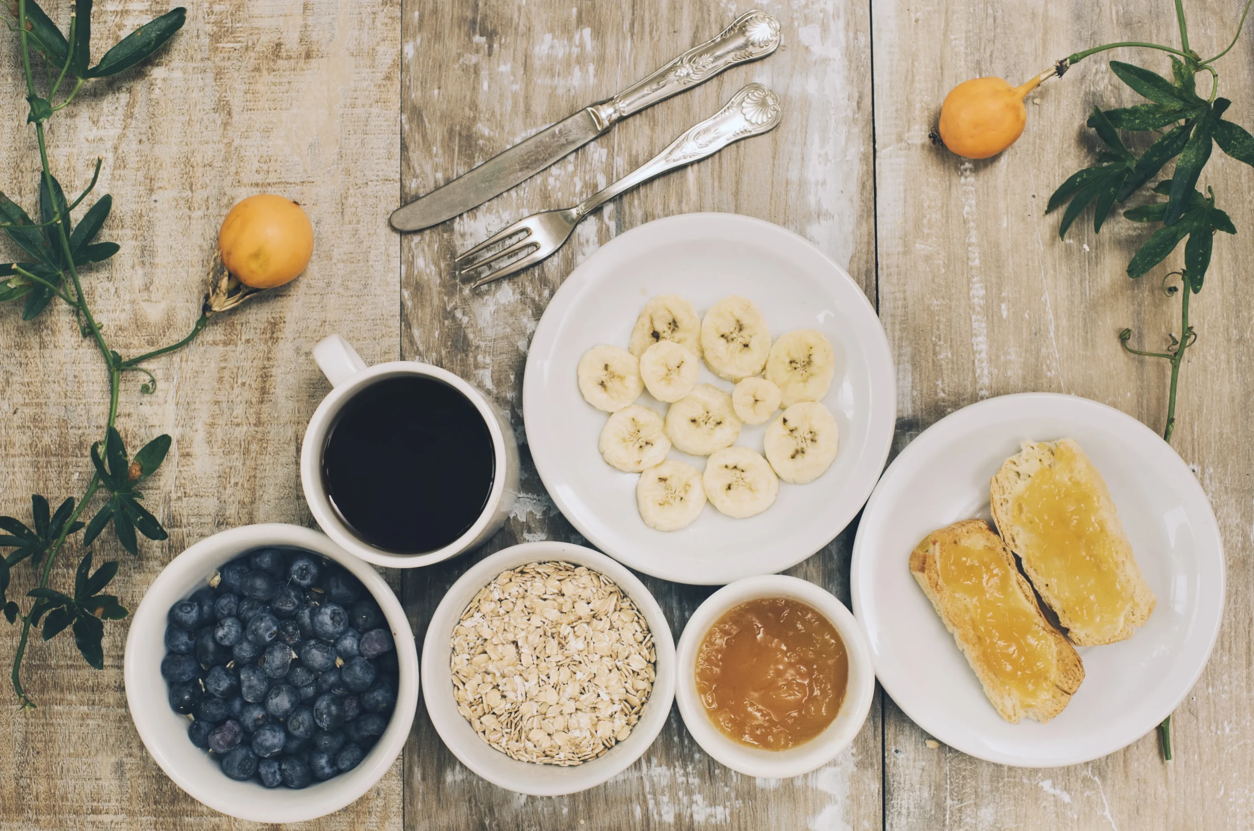 Gluten-free dairy-free breakfast with banana slices, blueberries, oats, jam, and toast on a rustic wooden table