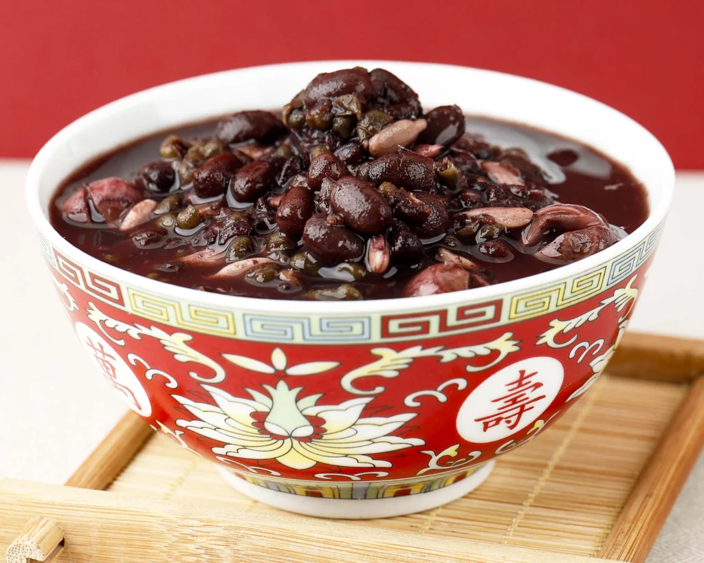 Purple black bean soup served in a decorative red bowl on a bamboo tray with a red background