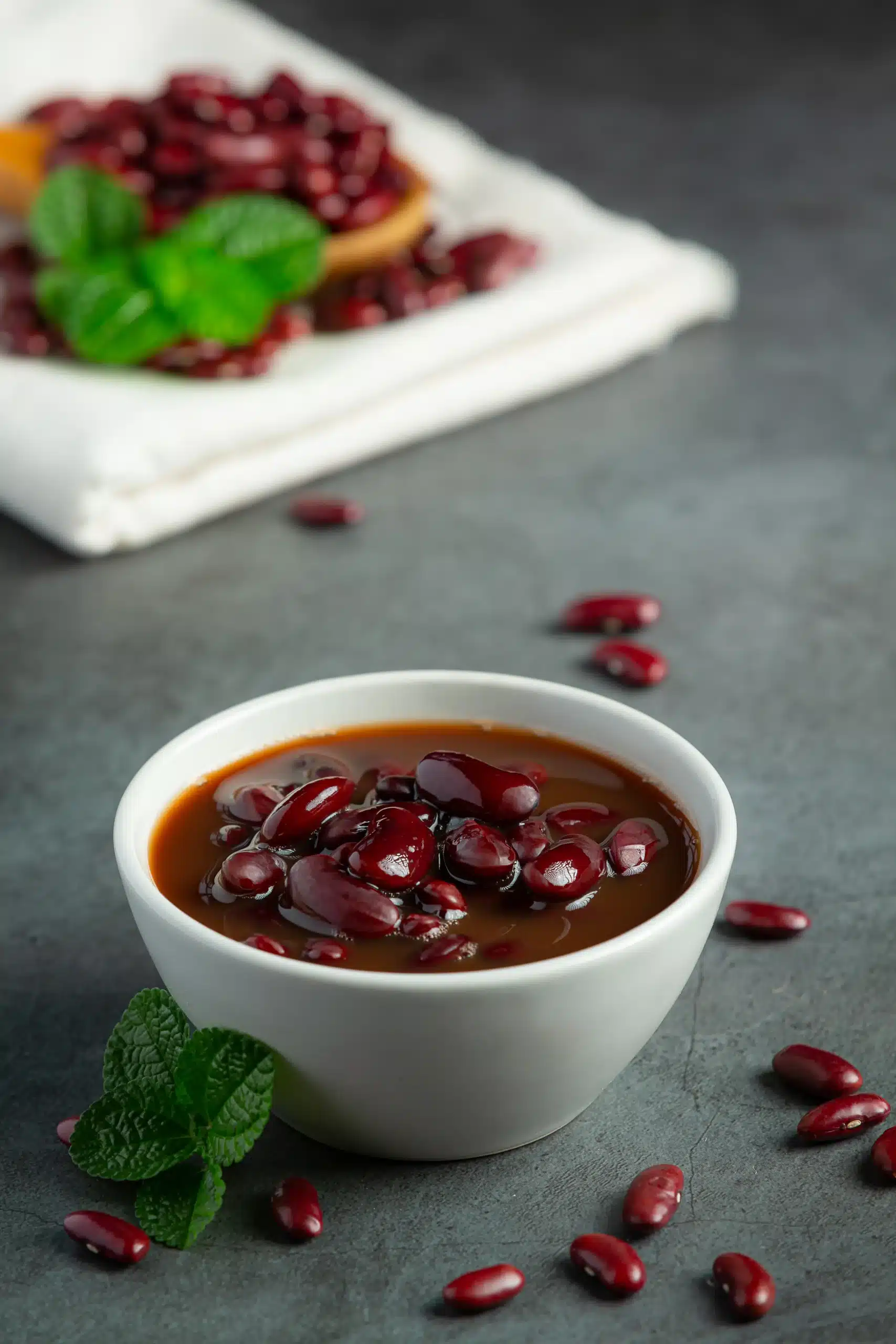 Cooked purple black beans in a white bowl with broth and fresh mint garnish on a dark surface