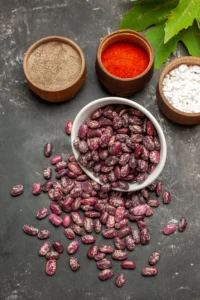 Raw purple black beans in a white bowl with seasonings on a dark surface