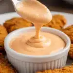 Spoonful of homemade Cane’s sauce over a dipping bowl with chicken tenders