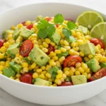 Fresh summer corn salad with avocado, cherry tomatoes, and lime in a white bowl.