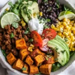 Overhead view of a colorful sweet potato taco bowl with roasted vegetables, seasoned beef, avocado, and fresh toppings