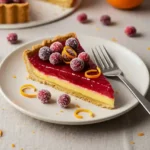 Slice of cranberry orange curd tart on dessert plate with sugared cranberries and zest garnish