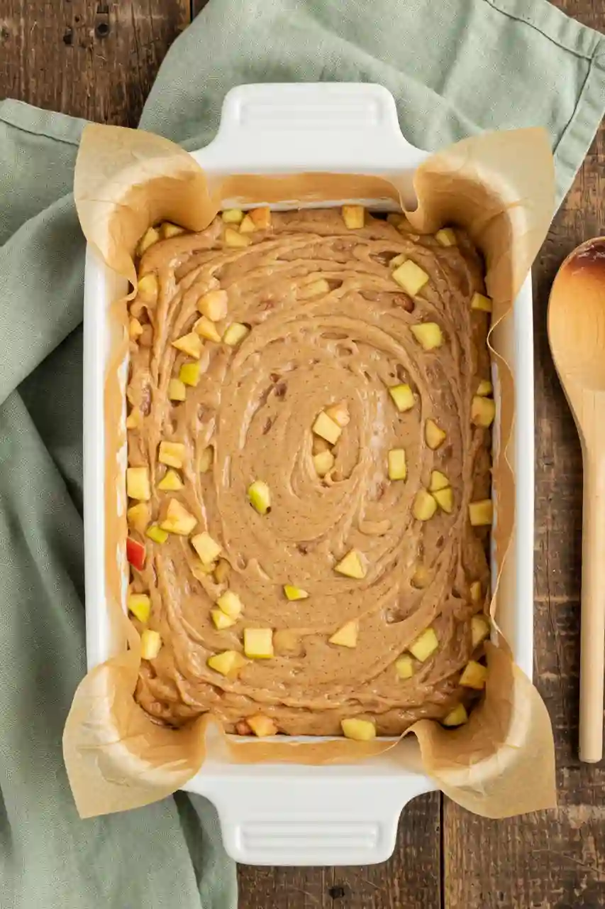 Preparing Blondie Batter with Apples Apple cinnamon blondie batter spread in a baking pan with apples