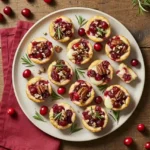 Overhead view of cranberry brie bites on a platter with red and sage holiday tones.